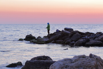 fisherman silhouette on the rocks against the background of sunset over the sea