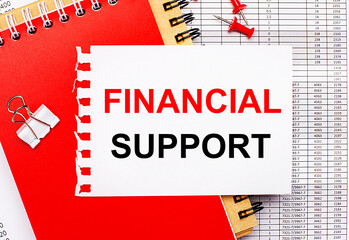 Against the background of the reports, there are red and brown notepads, a white paper clip, red buttons and a white sheet of paper with the text FINANCIAL SUPPORT. Business concept