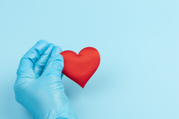 red heart in hands in blue medical gloves on a blue background. background for the day of the medic, top view, space for text