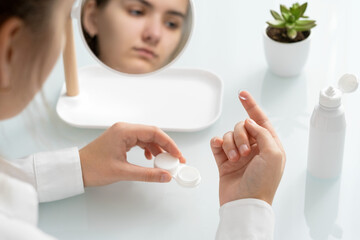 A young woman holds a contact lens on her finger