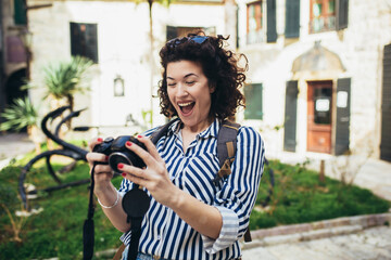 Outdoor summer smiling lifestyle portrait of pretty young woman having fun in the city in Europe in evening with camera travel photo of photographer