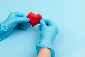 red heart in hands in blue medical gloves on a blue background. background for the day of the medic, top view, space for text