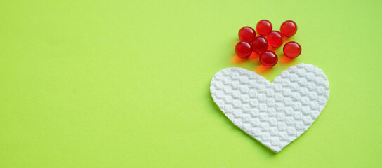 Red capsules and white heart on a green table