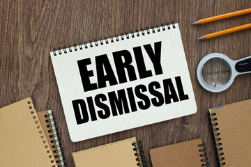 EARLY DISMISSAL Open notebook near a magnifying glass and pencils on wooden desk