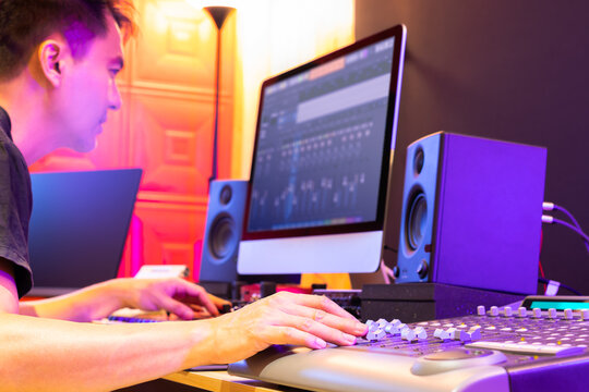 asian music producer, sound engineer, DJ hands mixing music tracks on digital mixer console in home recording studio. focus on hand. music production, recording concept