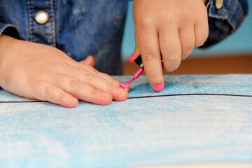 A little girl ineptly paints her nails with varnish from her mother's cosmetics.