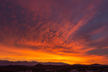 Bright dawn illuminated clouds by the sun orange light and mountain peaks in the distance.