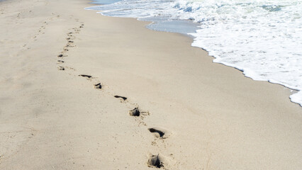 A lonely chain of footprints of one person on the sand on the seashore next to the rolling wave....