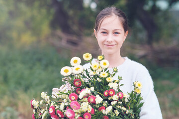 Portrait of a young girl holding a large beautiful bouquet of autumn flowers in her hands.