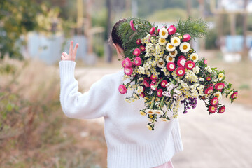 A young girl walks with a huge bunch of flowers behind her back and shows the victory sign with her...