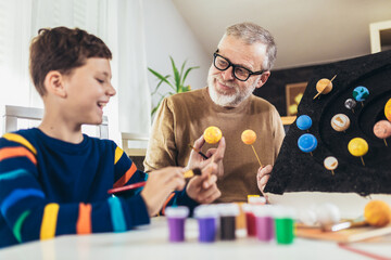 Happy school boy and his father making a solar system for a school science project at home