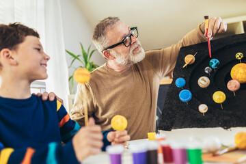 Happy school boy and his father making a solar system for a school science project at home