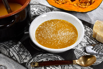 Pumpkin cream served in a bowl set on a table with pumpkin, pan, spoon and placemat