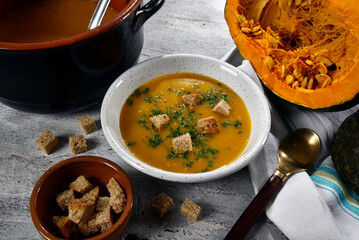 Pumpkin cream served in a bowl with croutons, set on a table with pumpkins and pan