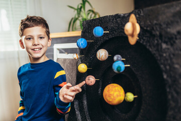 Happy school boy making a solar system for a school science project at home