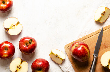 Red whole and sliced apples on a wooden board with a knife and a white napkin on a light background. 