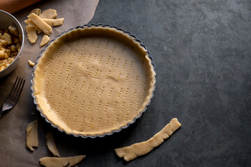 Homemade pie crust in pie plate. Cooking apple pie, dark background. Copy space - obrazy, fototapety, plakaty