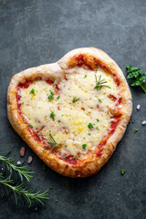 Homemade heart shaped pizza with sourdough dough and cheese for Valentine's Day on dark background. Top view, flat lay.