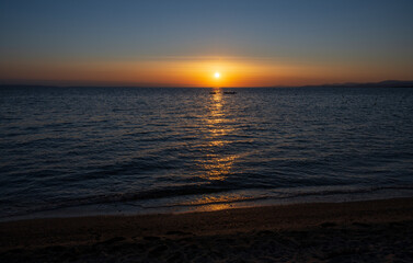 Teddy bear with red heart sits on the sunbed and watches sunset.	