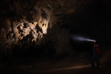 A male speleologist with helmet studying the walls of the dark cave