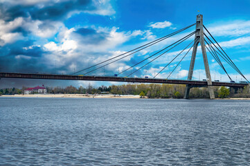 Fototapeta na wymiar Bridge over the Dnieper River in Kiev against a cloudy sky. Car crossing over water. Bridge over the river. Water flow. Blue sky. Thunderclouds. Background. Industrial architecture.