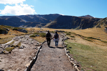 a man and a woman with backpacks are walking along a path in the mountains, rear view