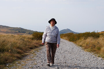 an elderly woman walks along the road against the backdrop of the mountains