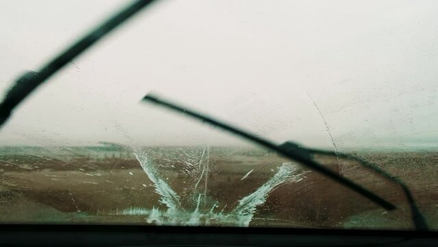 The view from the front window of the car with working windshield wipers during cold weather while moving.