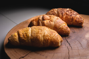Several Croissants on a cutting board made of sawn wood on a dark background. Healthy and tasty breakfast