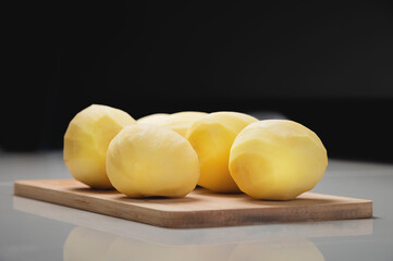 Peeled fresh potatoes on a wooden cutting board on a white table.