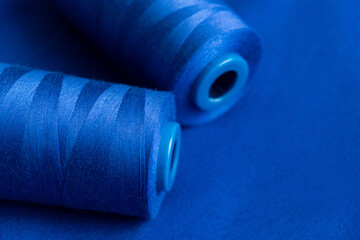 texture of blue thread in spool for sewing on a plain blue background. close up. clothing sewing...