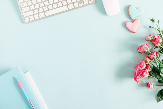 Composition Valentine's Day. Female desktop сomputer keyboard, notepad, rose flowers, ginger cookie in shape heart on pastel blue background. Valentine day concept. Flat lay, top view, copy space