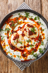 Cılbır is a Turkish dish of poached eggs with yogurt closeup in the plate on the wooden table. Vertical top view from above