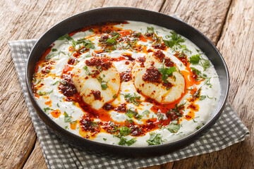 Cilbir is a Turkish eggs containing garlicky yogurt, poached eggs, and spiced melted butter in the plate on the wooden table. Horizontal