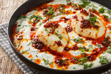 Turkish eggs or Cilbir are made with Greek yoghurt combined with fresh herbs and garlic closeup in the plate on the wooden table. Horizontal - obrazy, fototapety, plakaty