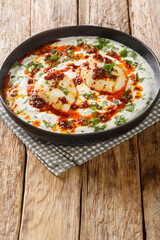 Cılbır is a Turkish egg dish reminiscent of a poached egg. prepared with yoghurt, garlic served with melted butter soaked in Aleppo pepper closeup in the plate on the wooden table. Vertical