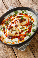 Cılbır is a Turkish dish of poached eggs with yogurt closeup in the plate on the wooden table. Vertical