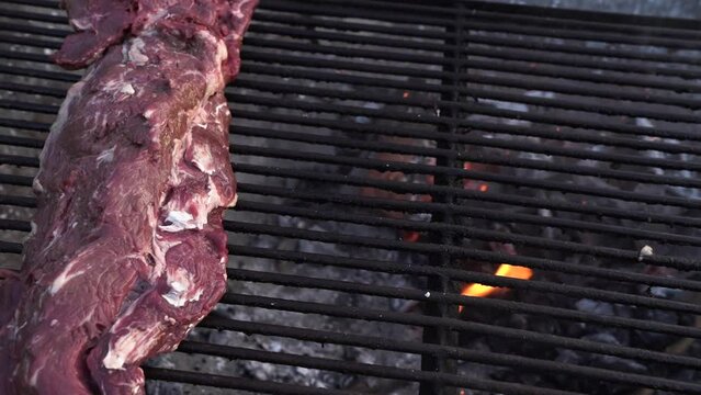 Barbecue outdoors. Panning red loin cooking in the the metal grill. The chef works the charcoal fire with grilling equipment. 