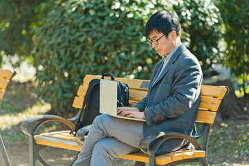 公園でノートパソコンを使う50代男性
