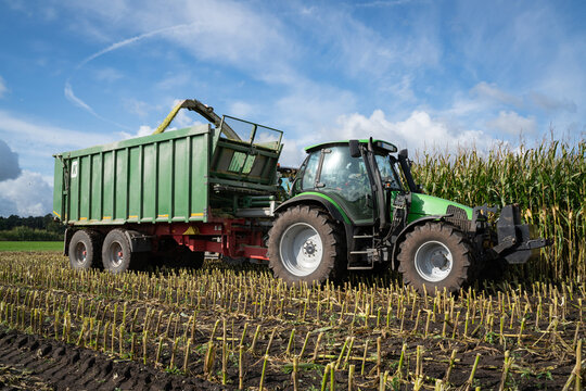 Maisernte -  Traktor mit Erntewagen fährt neben dem Häcksler her, um das Erntegut zu laden.