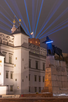 Vilnius Light Festival. Gediminas statue or star wars fighter with sword, at the Cathedral square with palace of the Grand Dukes of Lithuania and castle with rays laser lights in the sky and flag