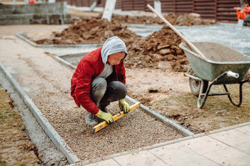 construction worker installing and laying pavement stones on terrace, road or sidewalk. Worker using pavement slabs and level to build stone sidewalk