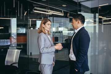 Two business partners have reached an agreement and shake hands, business people, Asian man and...