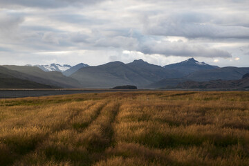 Fototapeta premium Paisaje con una bonita luz de atardecer, campo sembrado, montañas, nieva y nubes en Islandia.