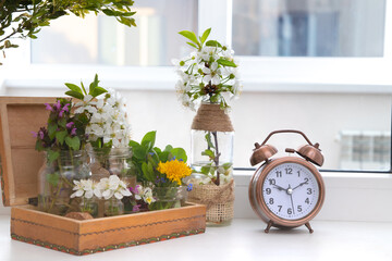 Alarm clock with flowering branches in a wooden box on the windowsill. Spring forward