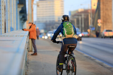 Mężczyzna jedzie  na rowerze z plecakiem po moście Grunwaldzkim we Wrocławiu.	
