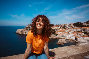 Laughing curly tourist walking on the old city walls of dubrovnik in croatia. Travel photography - obrazy, fototapety, plakaty