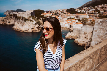 Fototapeta premium Laughing young woman tourist walking on the old city walls of dubrovnik in croatia overlooking the sea