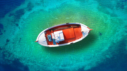 Aerial drone top down photo of beautiful red wooden traditional fishing boat anchored in crystal clear emerald sea near main old port of Mykonos island, Cyclades, Greece