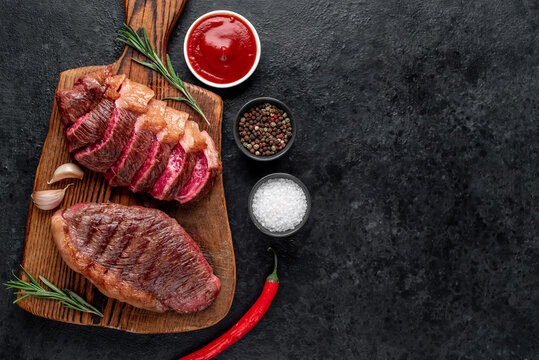 Two grilled picanha steaks with spices on a stone background